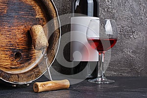 Red wine bottle with glass for tasting and wooden barrel with corkscrew in dark cellar