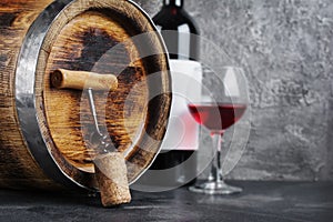 Red wine bottle with glass for tasting and wooden barrel with corkscrew in dark cellar