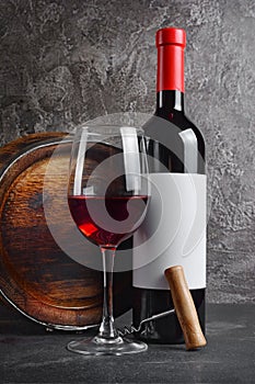 Red wine bottle with glass for tasting and wooden barrel in dark cellar