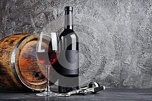 Red wine bottle with glass for tasting and wooden barrel in dark cellar