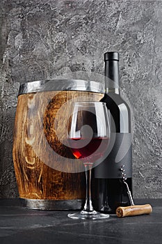 Red wine bottle with glass for tasting and wooden barrel in dark cellar