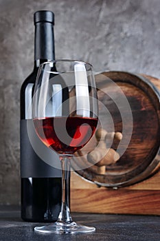 Red wine bottle with glass for tasting and wooden barrel in dark cellar