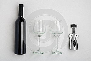 Red wine bottle, glasses and corkscrew over white background. Top view with copy space