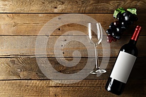 Red wine bottle with grapes and wine glass on brown rustic wooden table flat lay from above