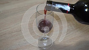 Red wine from a bottle is poured into a tall glass goblet.