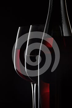 Red wine bottle and two wine glasses on black background