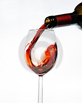 Red wine bottle upended and pouring its contents into a stemmed wine glass on a white background