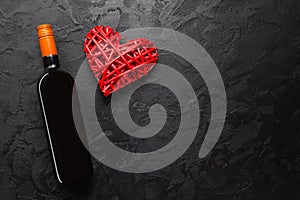 Red wine bottle with wicker decorative heart on black stone background. Valentines day love celebration. Copy space