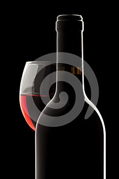 Red wine bottle and wine glass in a black backgrou