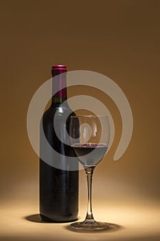 Red wine bottle and wine glass, placed on a warm brown background