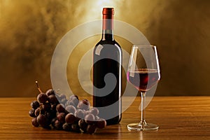 Red wine bottles with glass and grapes on wooden table and gold background