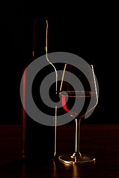 Red wine bottles and glass silhouette on wooden table and black background