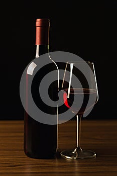 Red wine bottles and glass silhouette on wooden table and black background