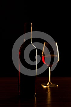 Red wine bottles and glass silhouette on wooden table and black background