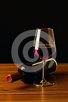 Red wine bottles and glass on wooden table and black background