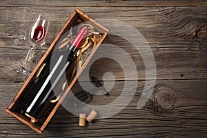 Red wine in a box with a glass and a corkscrew on a wooden table. Top view with space for your greetings