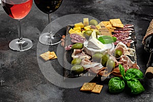 Red wine with charcuterie assortment Antipasto board with sliced meat, ham, salami, cheese, olives and wine on a dark background.