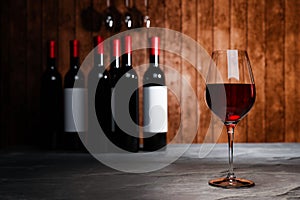 Red wine in clear glass, many blurred wine bottle backgrounds Place it on a cement floor with a wooden board wall. The cellar