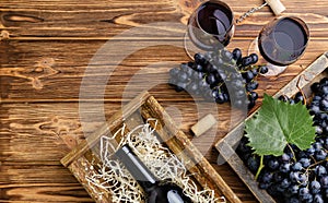Red Wine composition on brown wooden table. Top view. Red wine bottle corkscrew corks wine glasses black ripe grapes in box on