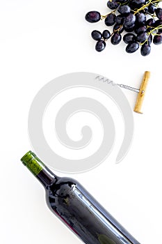 Red wine concept. Glass bottle with beverage near bunch of grapes and corkscrew on white background top view space for