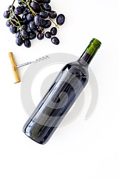 Red wine concept. Glass bottle with beverage near bunch of grapes and corkscrew on white background top view space for