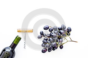 Red wine concept. Glass bottle with beverage near bunch of grapes and corkscrew on white background top view space for
