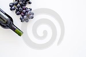 Red wine concept. Glass bottle with beverage near bunch of grapes on white background top view copy space