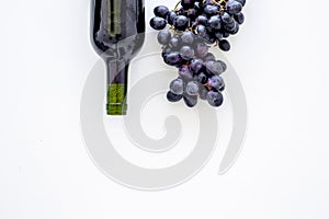 Red wine concept. Glass bottle with beverage near bunch of grapes on white background top view copy space