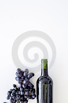 Red wine concept. Glass bottle with beverage near bunch of grapes on white background top view copy space