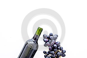 Red wine concept. Glass bottle with beverage near bunch of grapes on white background top view copy space