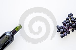 Red wine concept. Glass bottle with beverage near bunch of grapes on white background top view copy space