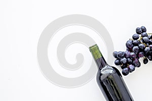 Red wine concept. Glass bottle with beverage near bunch of grapes on white background top view copy space