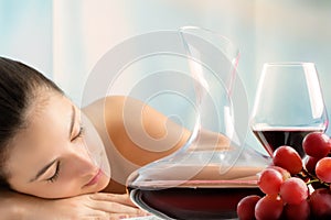 Red wine decanter and grapes with woman in background.