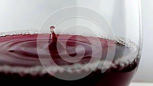 Red wine drop falling down into drink glass on white background, nutrition health-care concept, shooting with high speed camera