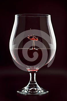 Red wine drop splashing inside glass close up