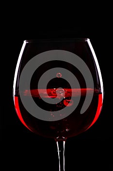 Red wine.Drops of wine fall in glass .Black background