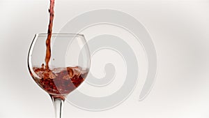 Red wine forms beautiful wave. Wine pouring in wine glass over white background. Close-up shot. Slow motion of pouring