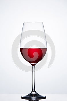 Red wine in the fragile pure wineglass standing against light bckground with reflection.