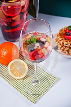 Red wine fresh sangria or punch with fruits, mint leaves and berries. Homemade waffles on the background