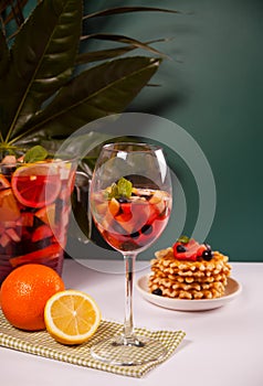 Red wine fresh sangria or punch with fruits, mint leaves and berries. Homemade waffles on the background