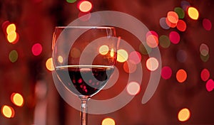Red wine glass against christmas lights bokeh background