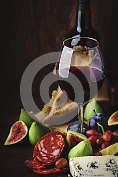 Red wine glass and appetizers, cheese, salami, figs, grapes, vintage wooden table background, selective focus, copy space