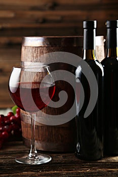 Red wine glass with bottle and barrel on a grey wooden background