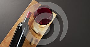 Red wine glass, bottle and cork lying on wooden board with copy space on black background