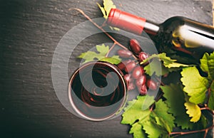 Red wine glass and bottle and fresh grapes on black background, focus on the wine glass