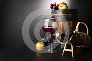 Red wine glass with bottle in sraw prop and old wooden barrel surrounded by fruits: vine and apples