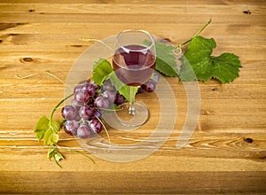 Red wine glass and bunch of grapes on wooden table