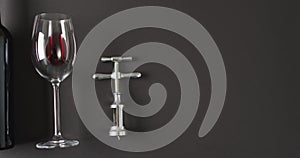 Red wine glass and corkscrew lying on black surface with copy space