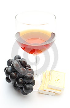 Red wine glass with grapes and cheese on white background