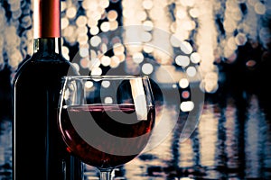 Red wine glass near bottle with light bokeh